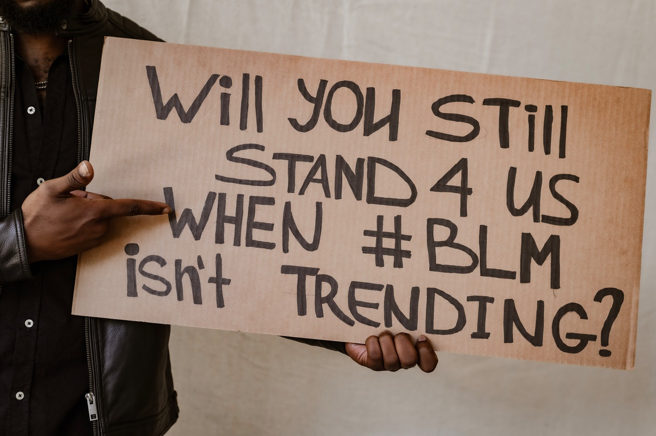 Person holding a cardboard sign that says "Will you still stand with us when #BLM isn't trending?"