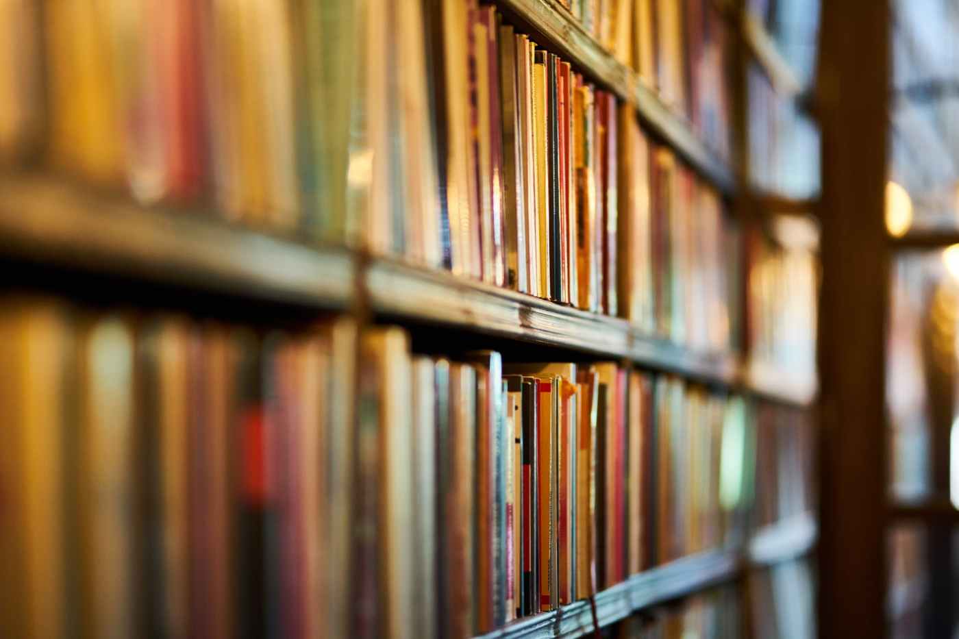 Looking down a long bookshelf with some of the bindings of the books in focus and others unclear