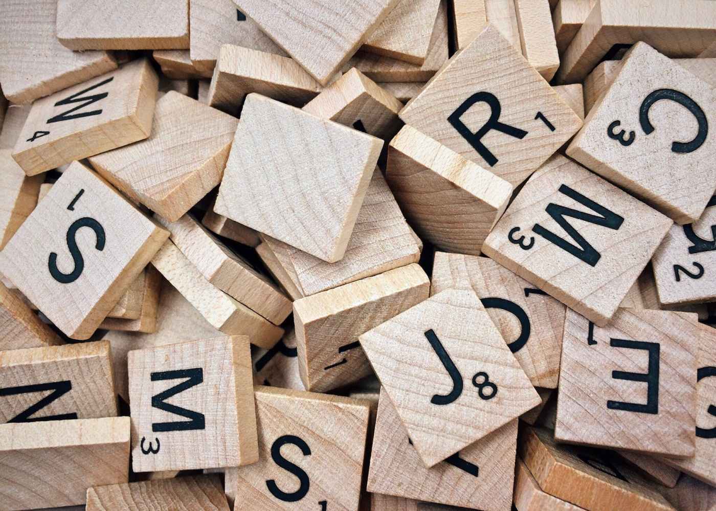 A jumbled pile of Scrabble letter tiles. Some have letters written on them, but many of the tiles are blank.